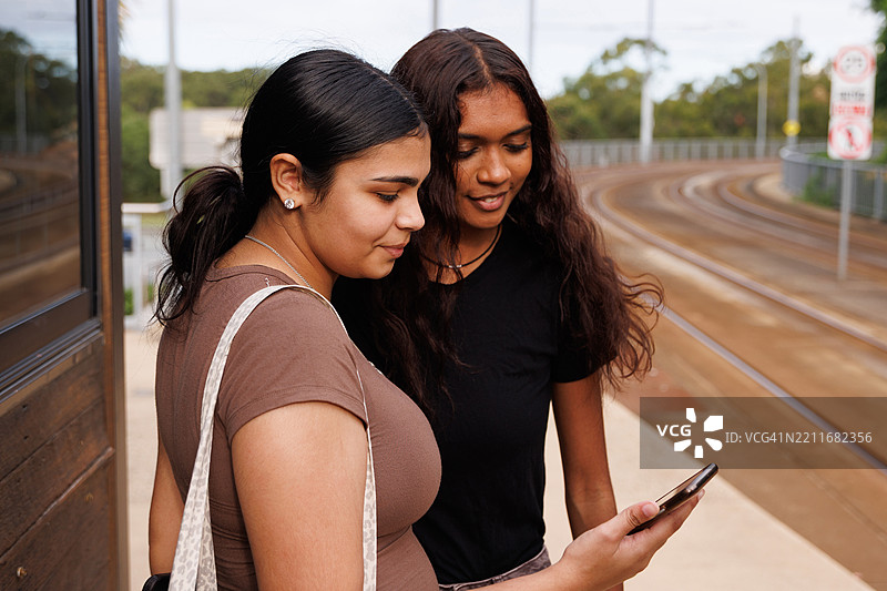 两个年轻的土著澳大利亚朋友在火车站查看手机图片素材