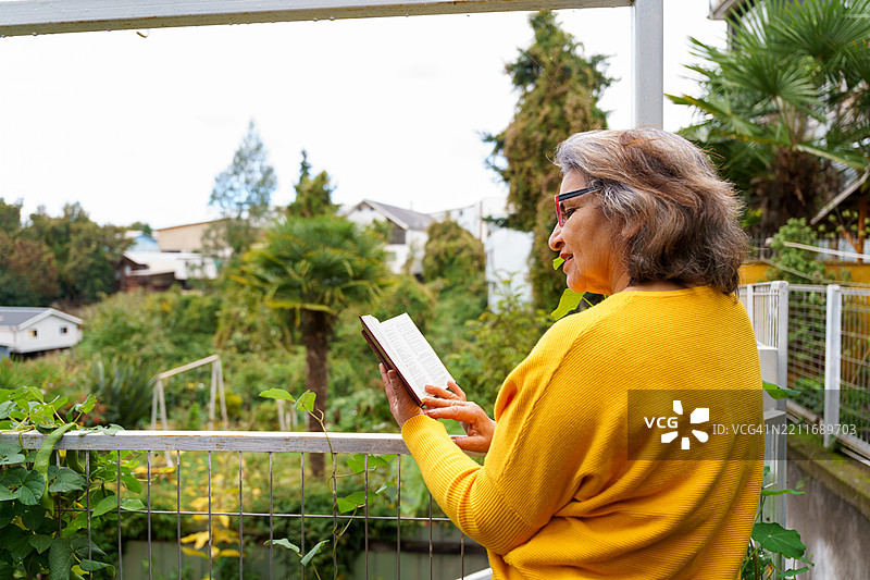 一位老年女性在阳台花园中阅读一本书图片素材
