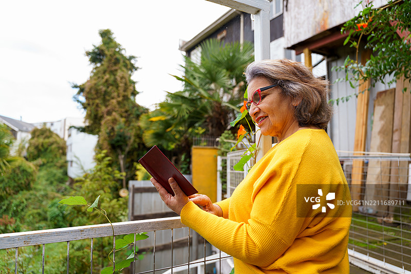 一位老年女性在阳台花园中阅读一本书图片素材