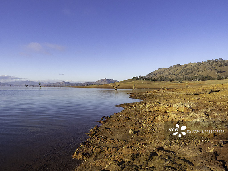 清晨的阳光洒在红色岩石地面上，旁边是宁静的湖泊图片素材