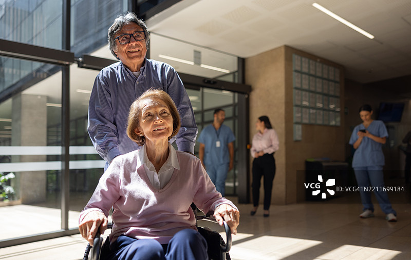 男子推着一位老年女性的轮椅，正抵达医院。图片素材