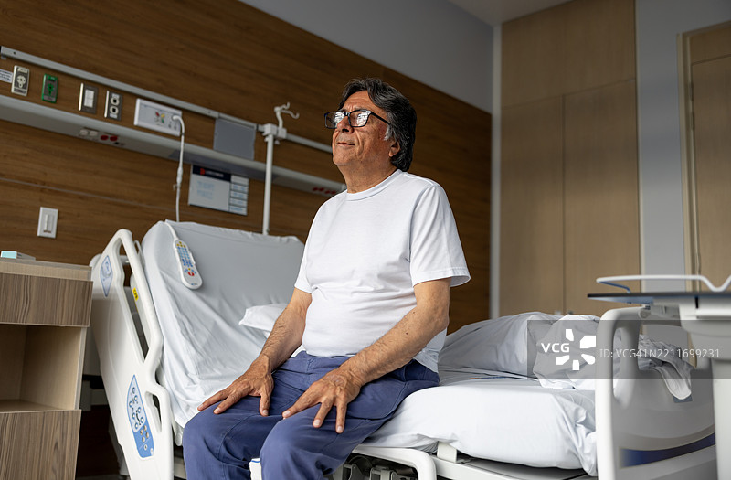 一位老年男子坐在床边，准备离开医院。图片素材
