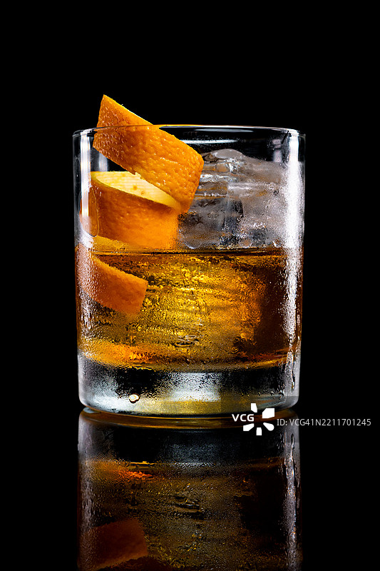 老式鸡尾酒加冰，装饰有螺旋橙皮，背景昏暗而富有情绪。图片素材