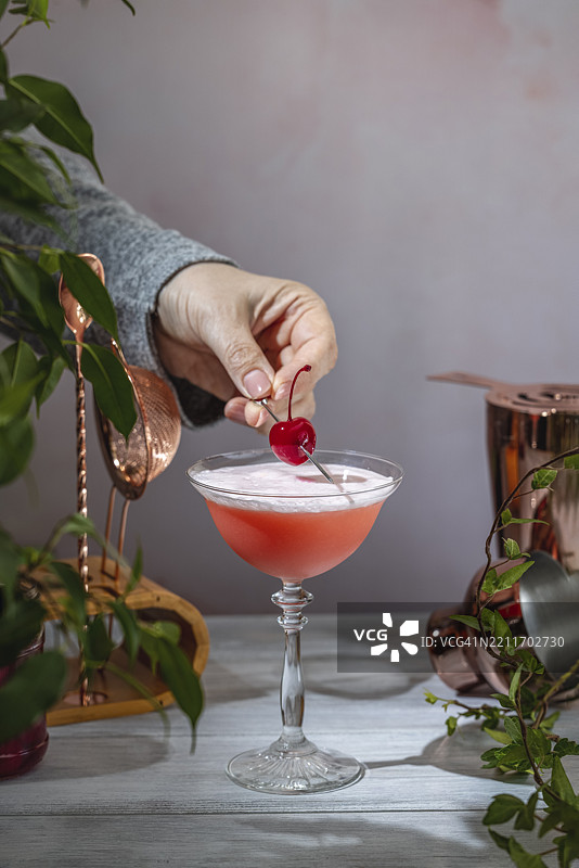 调酒师在粉色鸡尾酒上放置樱桃，鸡尾酒顶部泡沫丰富图片素材