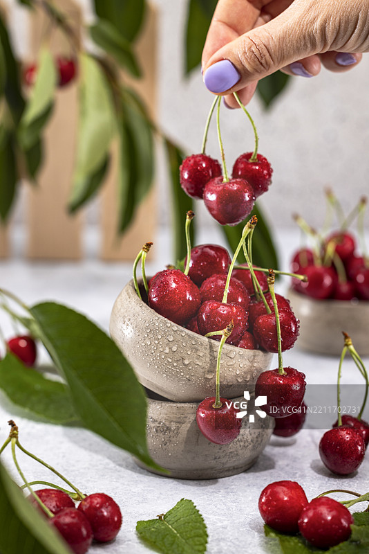 女人手持新鲜采摘的樱桃，放在乡村风格的碗上图片素材