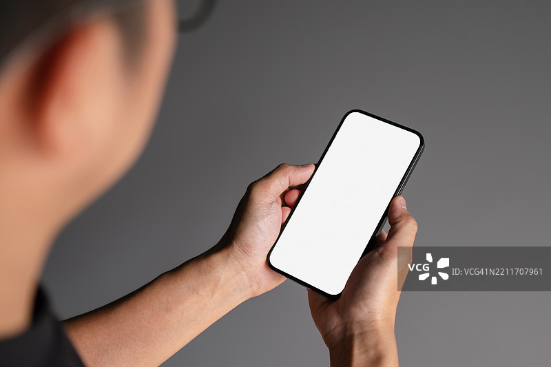 男人的手握着一部带有空白白屏的智能手机。图片素材