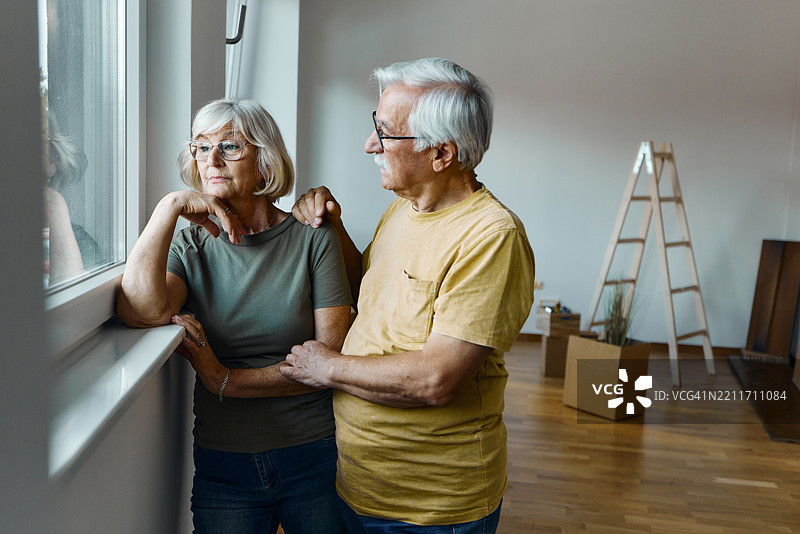 忧虑的成熟夫妇从他们的新公寓窗户向外望。图片素材