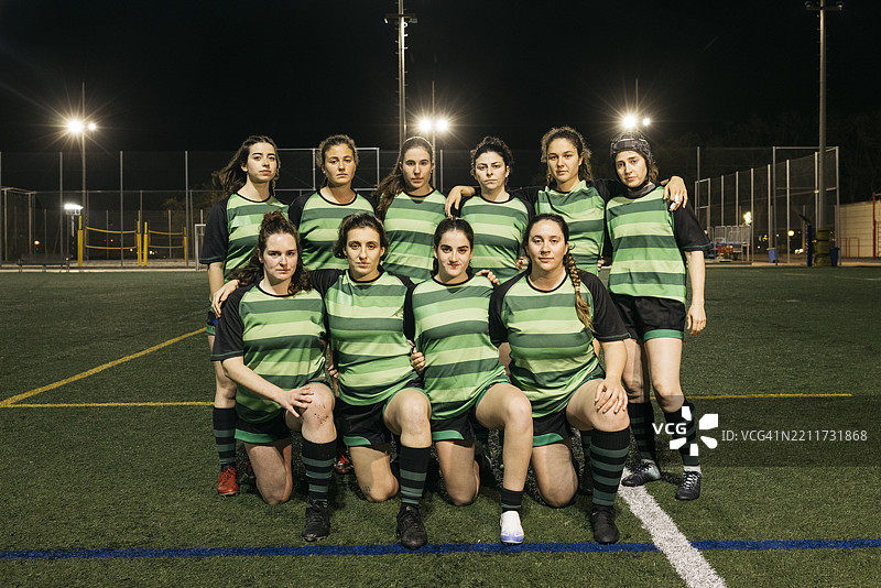 女子橄榄球队在夜间的球场上摆姿势合影图片素材