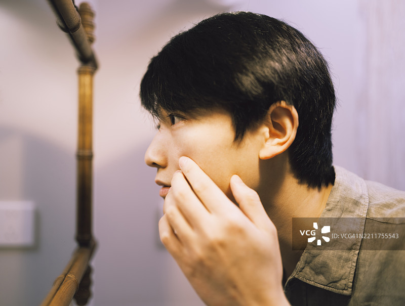 一位帅气的亚洲男子在浴室的镜子前检查自己的皮肤图片素材