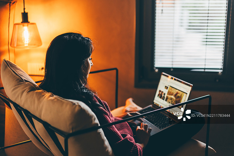晚上在家中使用笔记本电脑的女性肖像。图片素材