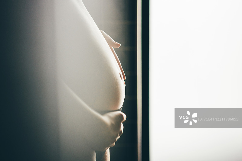 美丽的孕妇在家中拥抱着自己的肚子。图片素材