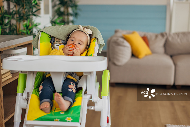 可爱的混血小女孩坐在客厅的高脚椅上，准备享用健康的水果零食图片素材