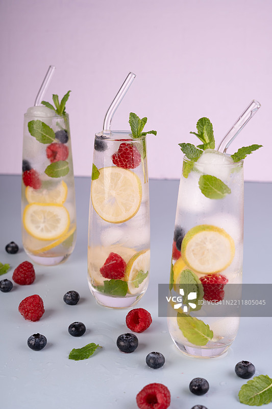 清澈的玻璃杯中盛放着柠檬片、覆盆子、蓝莓和薄荷叶，摆放在柔和色调的桌面上，营造出一种生动清新的氛围，视觉，节日，模板图片素材