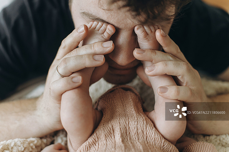 父亲节快乐，父亲在卧室里抱着新生儿的脚，爱与家庭的概念，爸爸与可爱的小婴儿玩耍，特写，收养，儿童健康与护理。图片素材