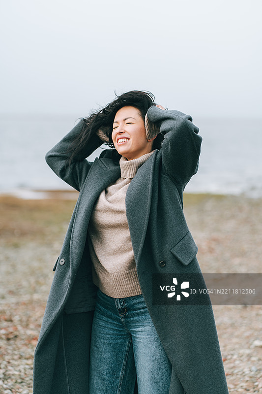 微笑的韩国女性在寒冷的海滩上捂住耳朵以抵御风寒图片素材