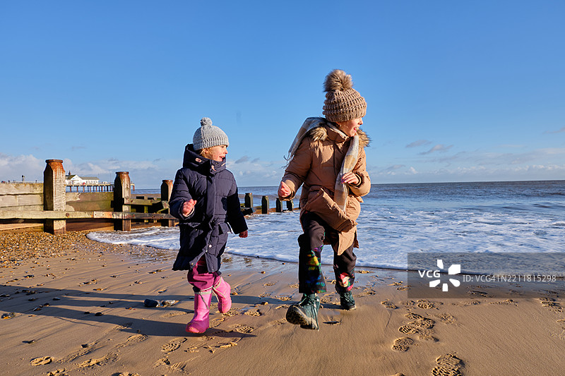两个姐妹在冬季海滩上奔跑 - 海边快乐的童年冒险图片素材