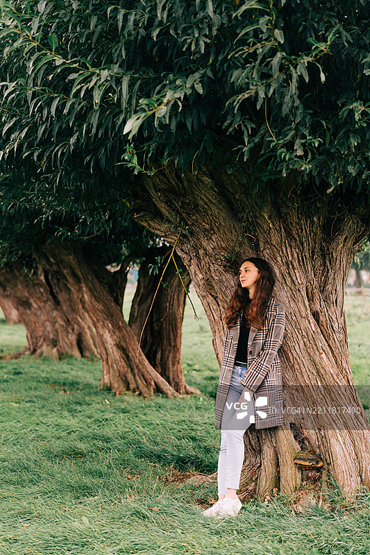 女人在风景如画的自然景观中靠树放松图片素材