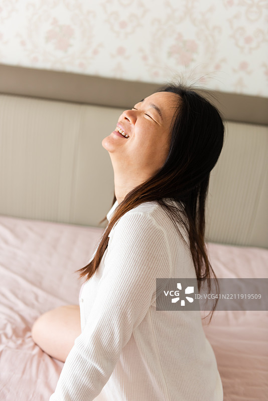 快乐的亚洲孕妇在床上大笑图片素材