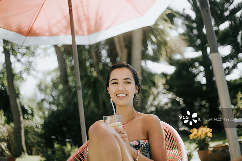 放松的西班牙裔年轻女性在夏季的户外露台上享受鸡尾酒图片素材