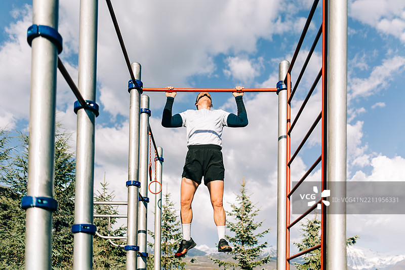 一个坚定的男人在蓝天下的健身公园里做引体向上。图片素材