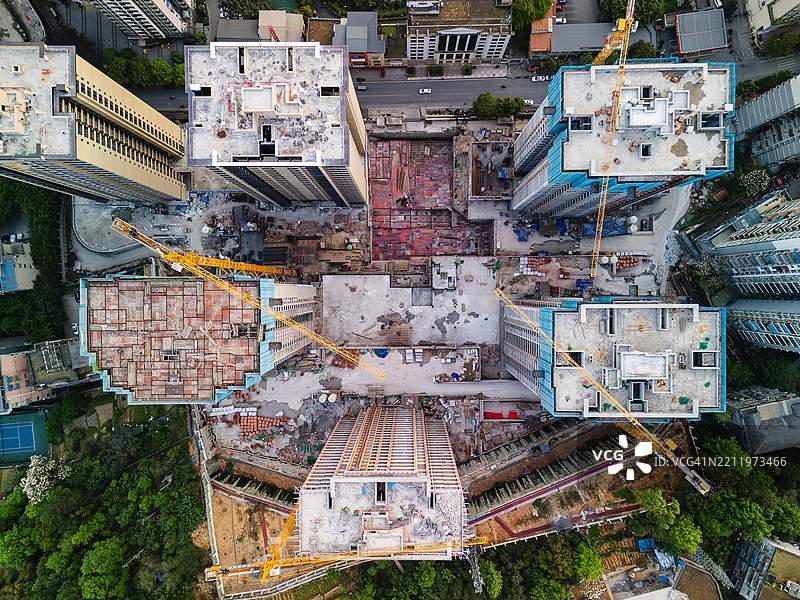 无人机拍摄的城市景观，俯视几座正在建设中的高层建筑，画面中有起重机、脚手架和周围的道路。图片素材