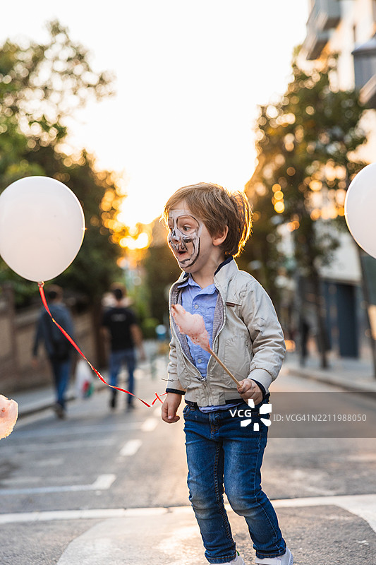 男孩脸上涂着彩妆，在社区节日上享受棉花糖和气球图片素材