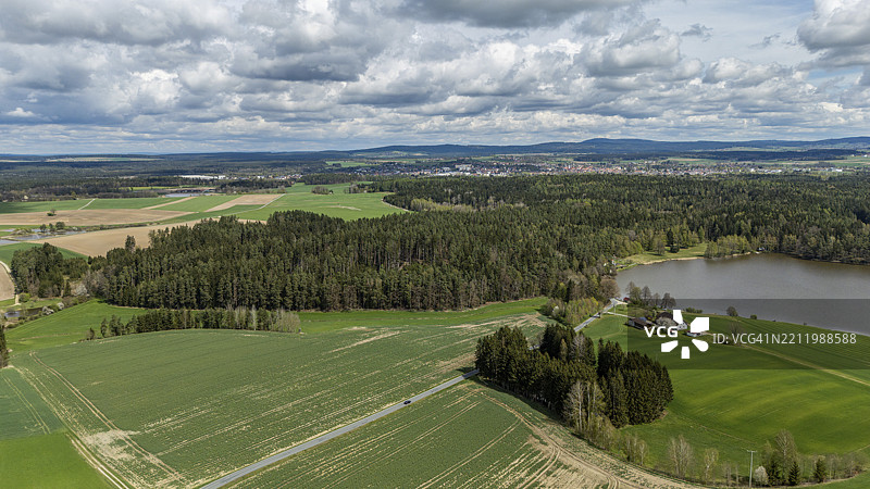 绿色的田野和湖泊环绕着森林，天空多云，位于德国巴伐利亚州上普法尔茨的提尔申罗伊特。图片素材
