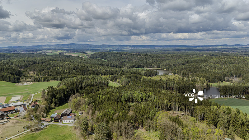 德国巴伐利亚上普法尔茨地区蒂尔申罗伊特的丘陵环境中，密林景观与田野和多云的天空。图片素材