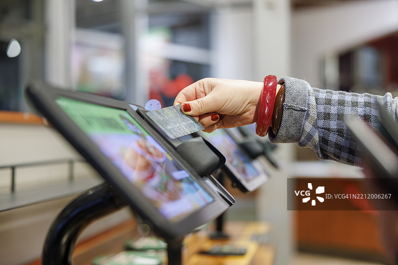 自助服务终端的卡片支付。佩戴红色手链的购物者在选择性焦点中完成购买。图片素材