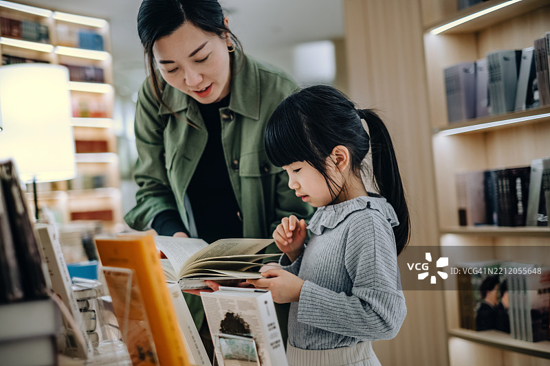 年轻的亚洲母亲和女儿在书店一起阅读书籍。鼓励孩子养成良好的阅读习惯。教育和学习理念。图片素材