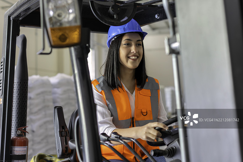 年轻女性叉车司机在仓库内操作叉车时微笑图片素材