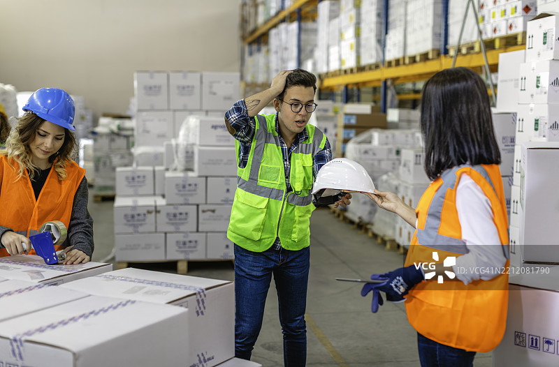 穿着安全装备的仓库工人在仓库中讨论并搬运箱子图片素材