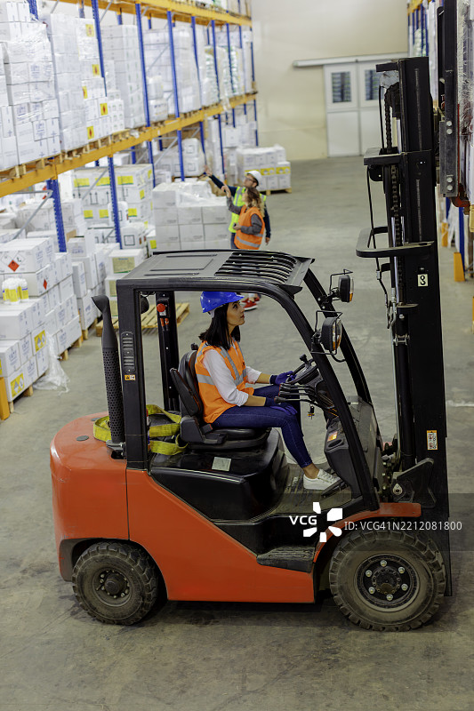 女性叉车司机在仓库中驾驶叉车，背景有另一名工人。图片素材