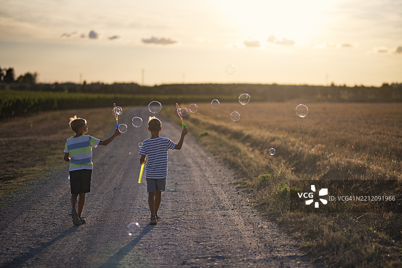 两个男孩在阳光明媚的乡间小路上吹泡泡图片素材