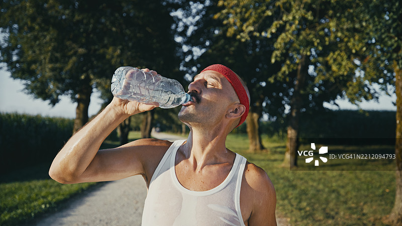 中年男子穿着白色背心在户外锻炼时喝水图片素材
