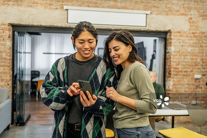 微笑的同事们在现代办公室使用智能手机图片素材