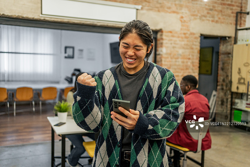 年轻人在共享办公空间用智能手机庆祝成功图片素材