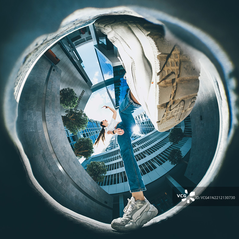 一位年轻女子以广角、低角度的视角被捕捉到，在现代城市建筑之间充满活力地跳跃。图片素材