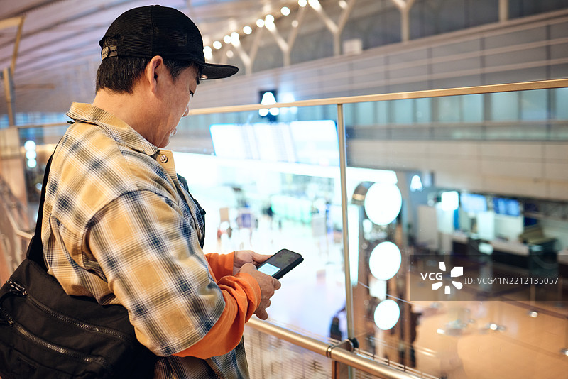 老年男子在城市阳台的玻璃围栏上使用智能手机。图片素材