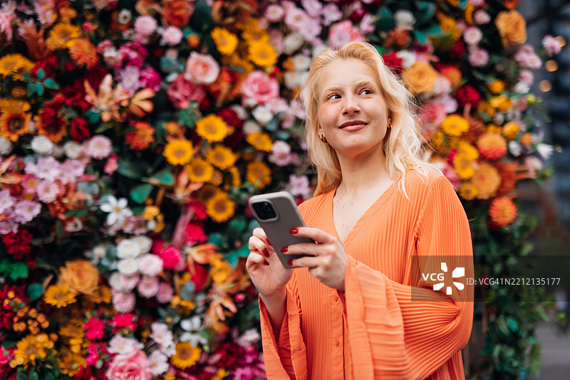 年轻女性在五彩缤纷的花墙前使用智能手机图片素材
