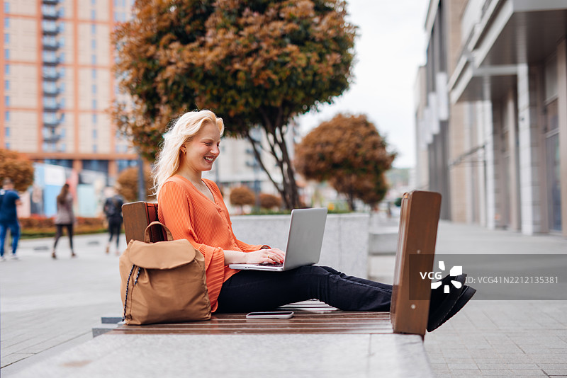 年轻学生坐在大学校园的长椅上使用笔记本电脑。图片素材