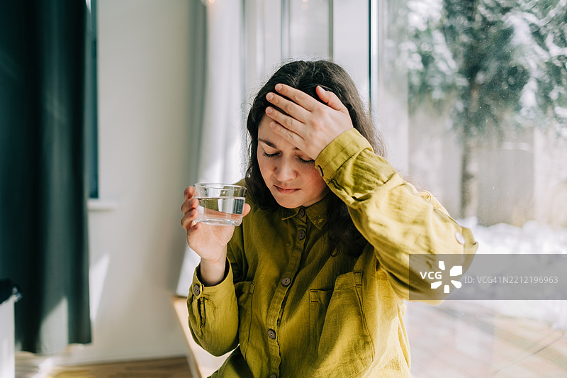 女人拿着一杯水，感到头痛不适。图片素材