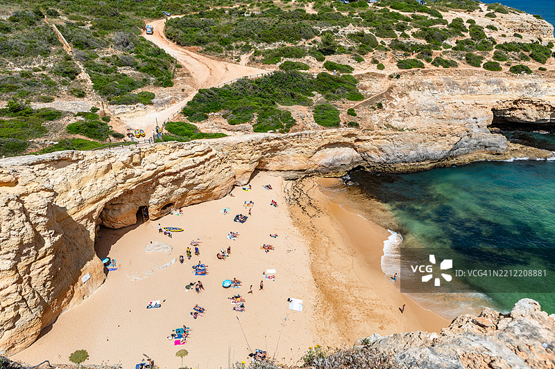 俯瞰在隐秘的金色沙滩上晒太阳的人们，清澈的海洋被悬崖环绕，位于葡萄牙卡尔沃埃罗的卡尔瓦略海滩。图片素材