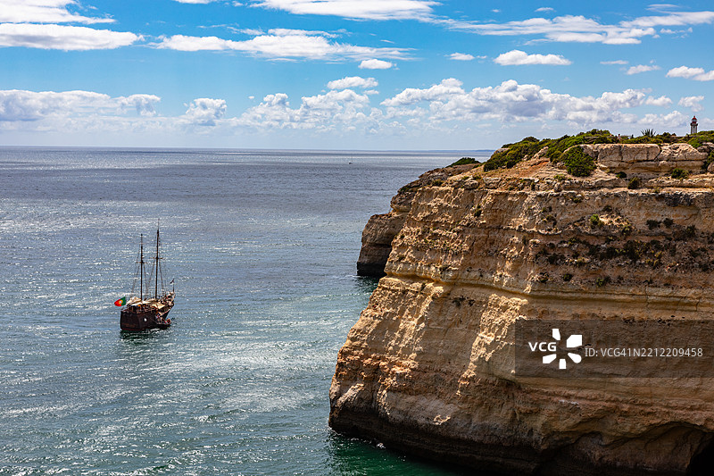 在平静的大西洋上，一艘卡拉维尔帆船在石灰岩悬崖旁航行。图片素材
