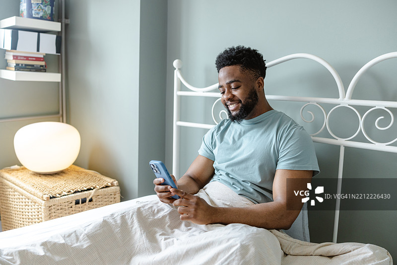 男人躺在床上，面带愉悦表情看着智能手机。图片素材