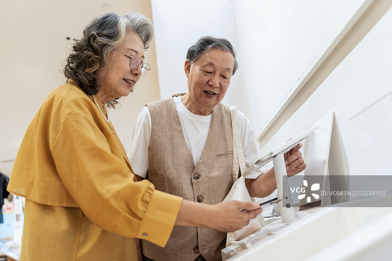 亚洲老年夫妇在服装店一起挑选新衣服，并使用她的智能手机进行移动支付。图片素材