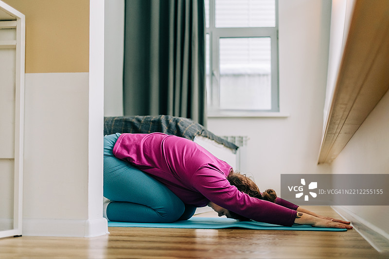 女人在卧室的瑜伽垫上做儿童式瑜伽。图片素材