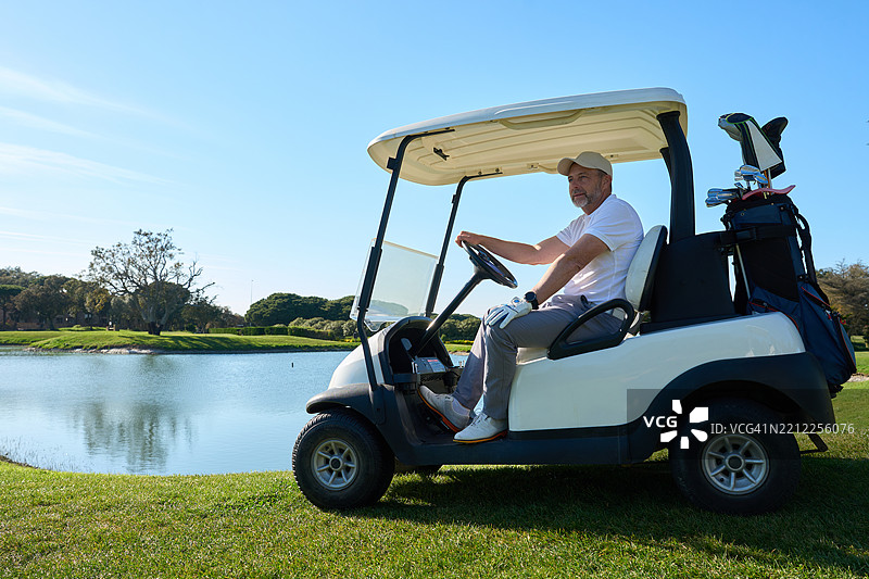高尔夫球手在阳光明媚的日子里驾驶高尔夫球车在湖边。图片素材