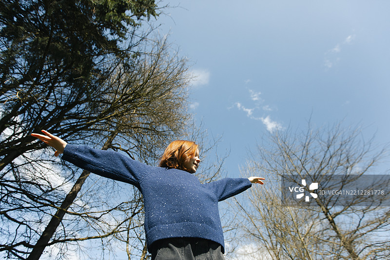 低角度视图的红发女孩在森林中伸展双手并站立图片素材