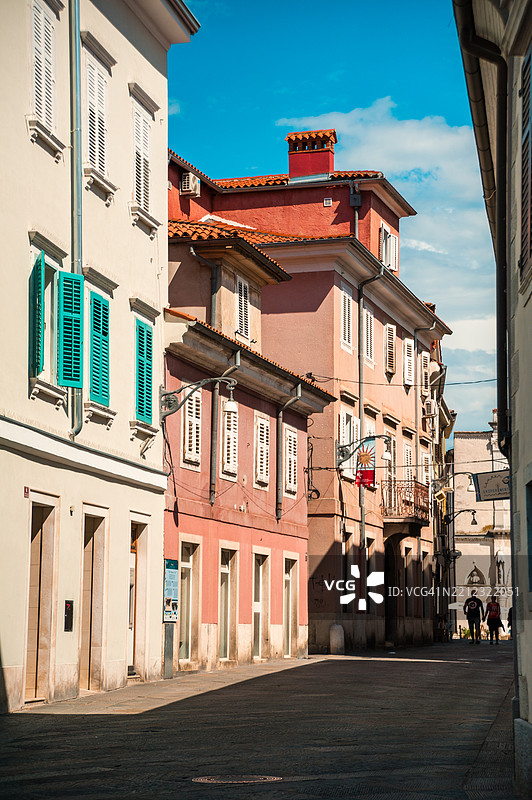两个人在老城区的街道上散步，街道两旁是传统和历史悠久的住宅建筑。图片素材